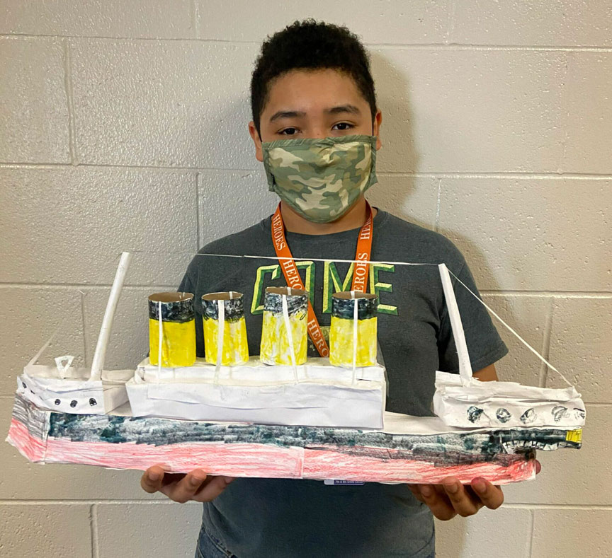 A picture of a boy holding their Titanic-inspired paper sculpture.