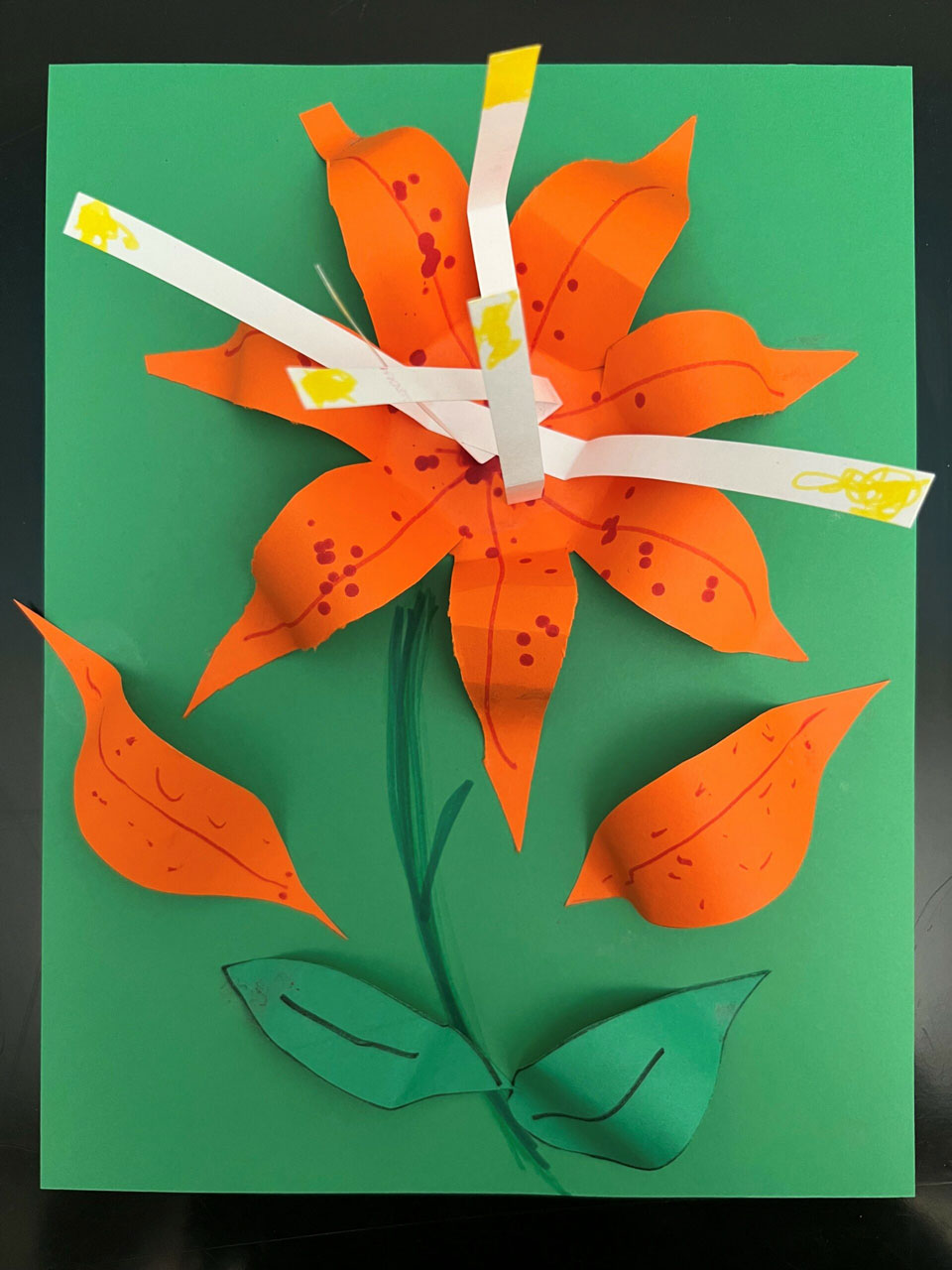 An orange 3D paper lily flower on a green background.