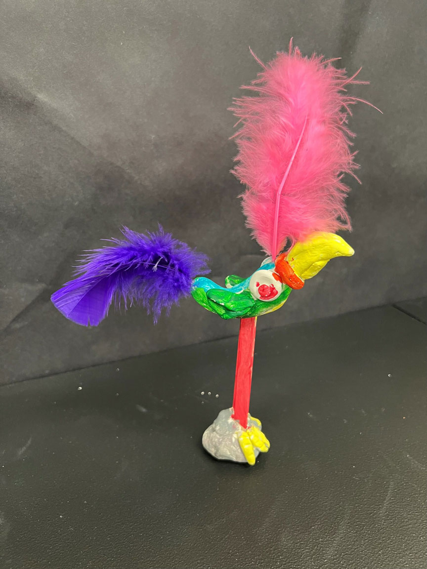 A clay sculpture of a green and blue exotic bird, with multicolored feathers.