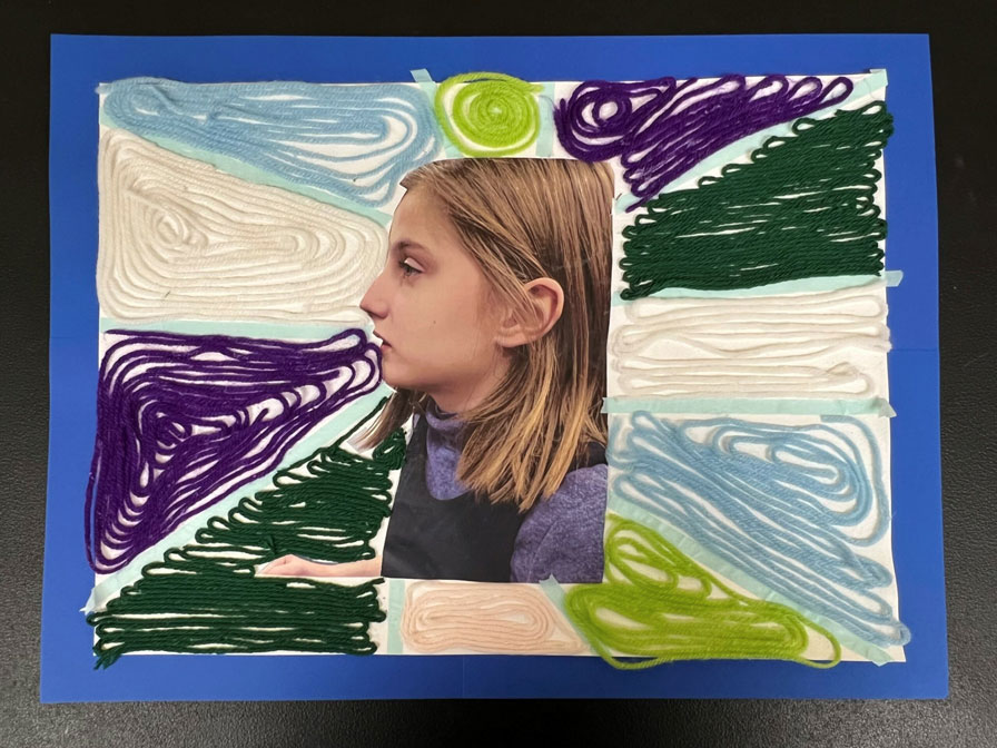 A white, purple, green and blue yarn-based ray artwork with a girl's picture in the middle. 