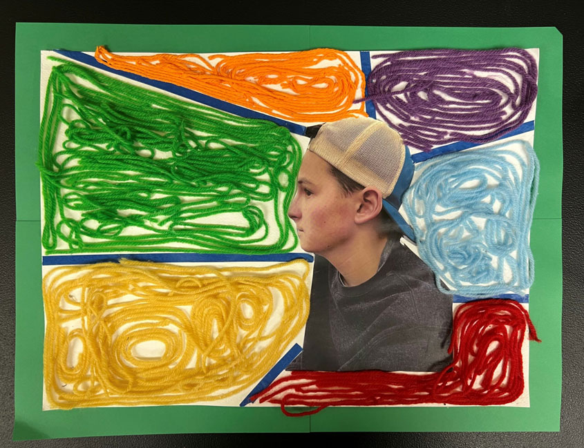 A rainbow yarn-based ray artwork with a boy's picture in the middle. 