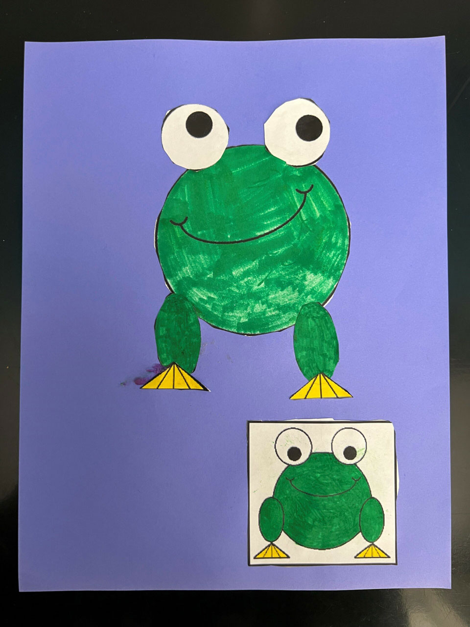 A green marker colored in paper frog glued onto a purple paper for its background.